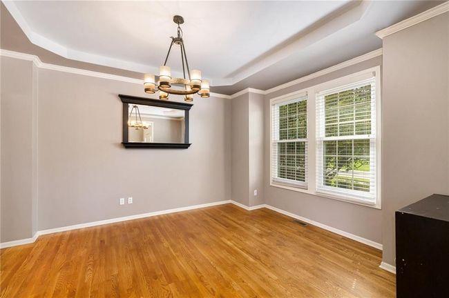 Empty room with a raised ceiling, a chandelier, wood finished floors, and baseboards | Image 7