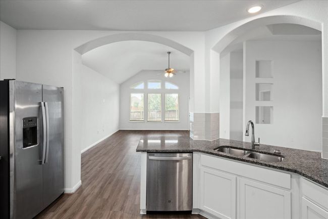 Kitchen with stainless steel appliances, a sink, dark stone countertops, ceiling fan, and lofted ceiling | Image 11