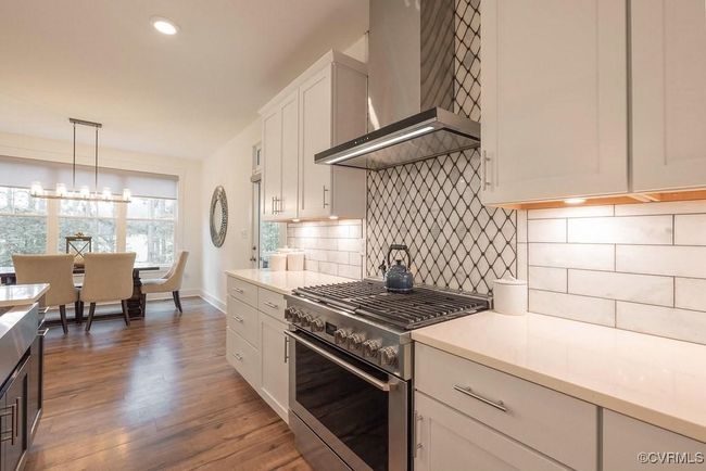 Kitchen featuring high end stainless steel range, wall chimney range hood, light countertops, white cabinetry, and recessed lighting | Image 30
