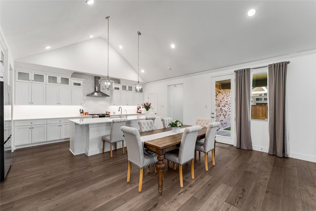 Kitchen with wall chimney exhaust hood, stainless steel gas range, a kitchen bar, white cabinets, and an island with sink | Image 4
