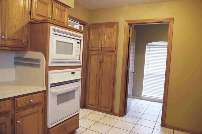 Kitchen featuring white appliances, brown cabinets, light tile patterned floors, and light countertops | Image 7