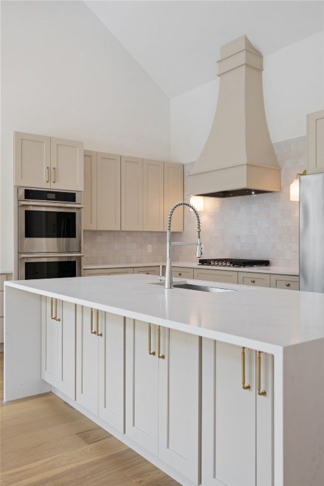 Kitchen featuring custom range hood, stainless steel appliances, a sink, light countertops, and backsplash | Image 12