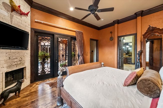 Bedroom with crown molding, access to exterior, wood finished floors, a fireplace, and ceiling fan | Image 23