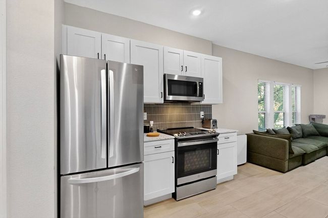 Kitchen with stainless steel appliances, open floor plan, tasteful backsplash, and white cabinets | Image 16
