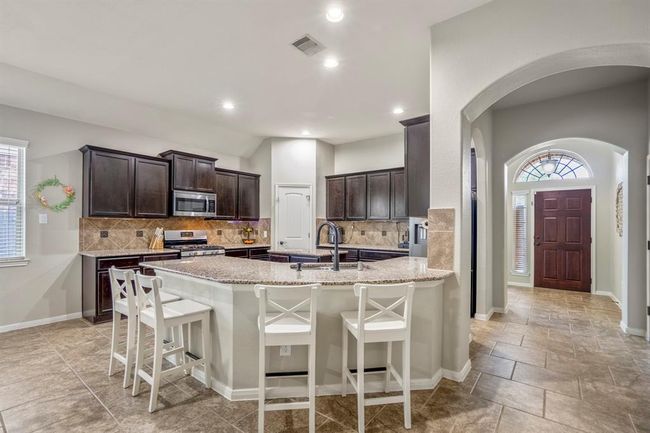 As you move deeper into your future home, glance back through graceful arches toward the front door, while the spacious kitchen welcomes you on the left—highlighting the open flow that makes daily life easy and connected. | Image 7
