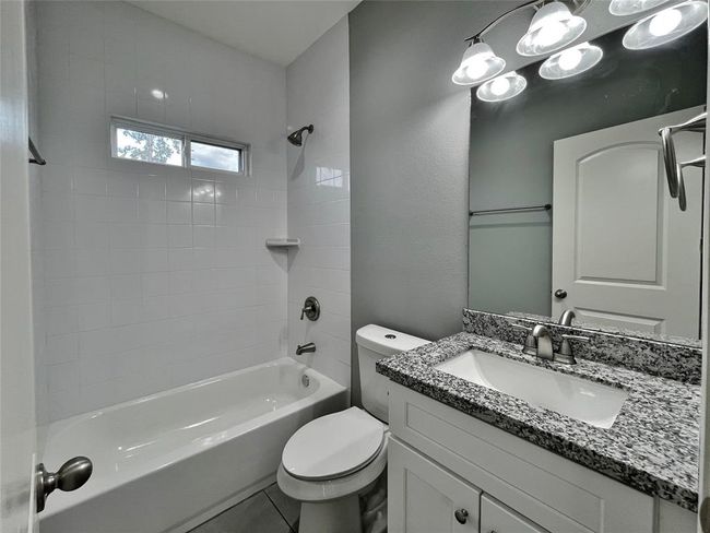 This bathroom features a modern design with a granite countertop, white cabinetry and a bathtub/shower combo. The natural light creates a bright and inviting space. | Image 15