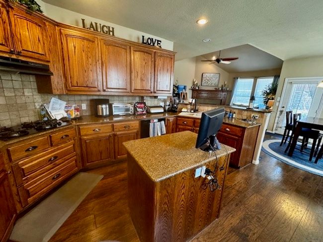 Kitchen with dark wood-style floors, a peninsula, brown cabinets, and a ceiling fan | Image 4