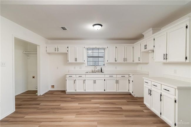 Kitchen with light wood-type flooring, white cabinets, visible vents, and a sink | Image 4