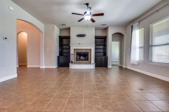 Unfurnished living room with arched walkways, a tiled fireplace, ceiling fan, and light tile patterned floors | Image 6