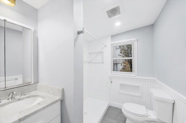 Full bathroom featuring toilet, vanity, tiled shower, a wainscoted wall, and tile patterned floors | Image 13