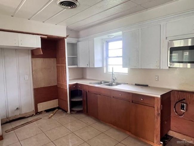 Kitchen with stainless steel microwave, light countertops, white cabinets, and light tile patterned floors | Image 11