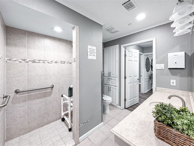 Bathroom featuring a textured wall, tile patterned flooring, crown molding, vanity, and tiled shower | Image 33