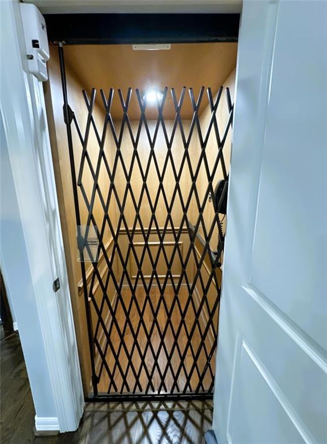 This photo shows a home elevator with a wooden interior and a metal accordion gate, providing convenient access between floors. | Image 14