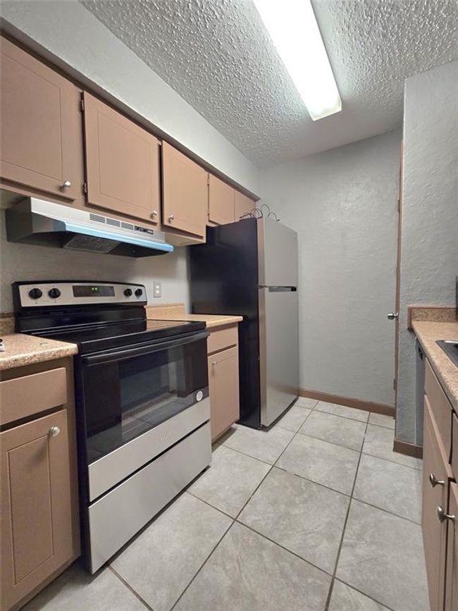 Cozy galley kitchen with modern appliances, ample cabinetry, and neutral tones. Ideal for efficient cooking and storage. | Image 15