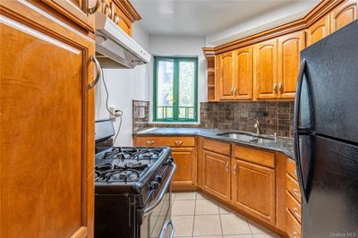 Kitchen with black appliances, light tile patterned floors, range hood, sink, and decorative backsplash | Image 2