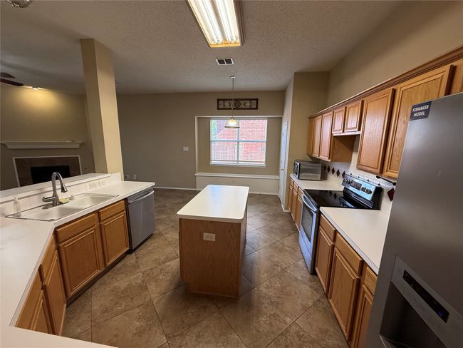 Kitchen with stainless steel appliances, a sink, a center island, brown cabinetry, and a textured ceiling | Image 9