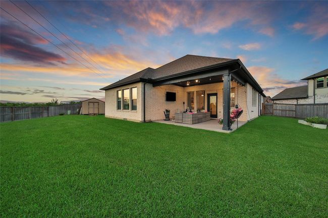 This photo showcases a modern brick home with a spacious backyard, featuring a covered patio area perfect for outdoor lounging and entertainment. The well-maintained lawn and vibrant sky enhance the inviting atmosphere. | Image 4