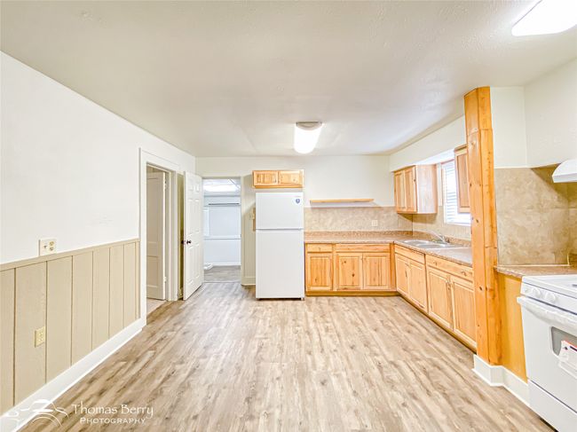 Kitchen with white appliances, light wood finished floors, light brown cabinets, light countertops, and a wainscoted wall | Image 10