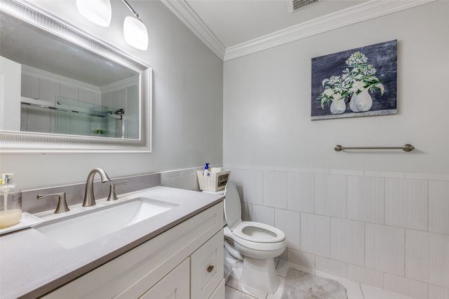 Full bathroom with tile walls, ornamental molding, vanity, a shower with shower door, and tile patterned floors | Image 16