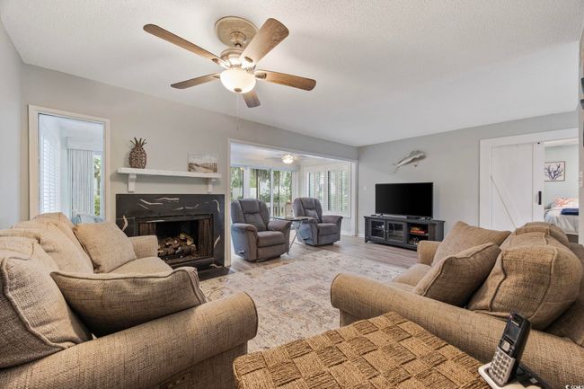 Living area featuring a ceiling fan, a fireplace with flush hearth, wood finished floors, and a textured ceiling | Image 18