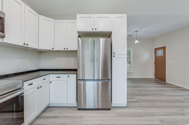 Kitchen featuring stainless steel appliances, white cabinetry, light wood-type flooring, dark countertops, and baseboards | Image 11