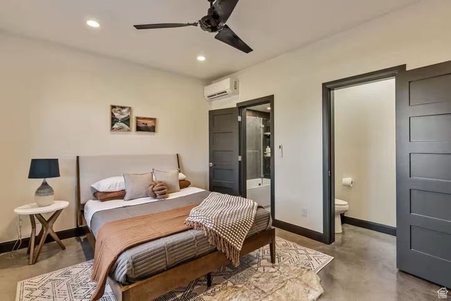 Bedroom with a wall unit AC, recessed lighting, concrete floors, baseboards, and ensuite bath | Image 54