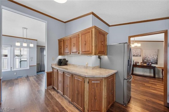 Kitchen featuring dark wood-style flooring, stainless steel refrigerator with ice dispenser, brown cabinets, and crown molding | Image 10