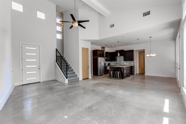 Unfurnished living room with concrete flooring, stairs, baseboards, and ceiling fan with notable chandelier | Image 4