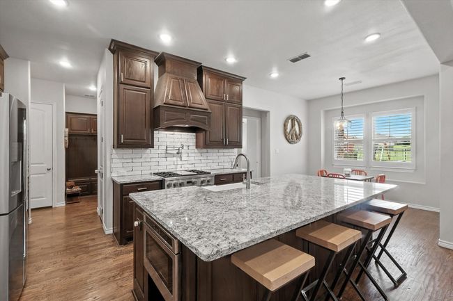 Kitchen with premium range hood, appliances with stainless steel finishes, decorative backsplash, a kitchen bar, and light stone counters | Image 13