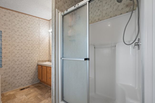 Bathroom with a stall shower, vanity, stone finish flooring, crown molding, and wallpapered walls | Image 20