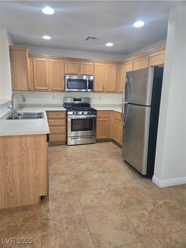 Kitchen with stainless steel range with gas cooktop, a sink, fridge, visible vents, and light countertops | Image 5