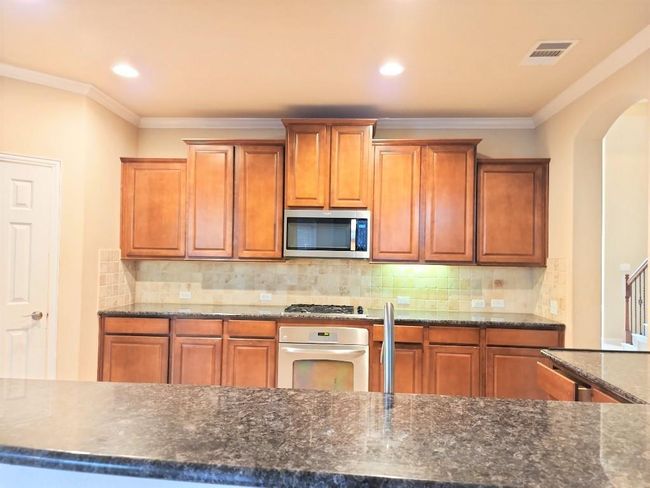 Kitchen with appliances with stainless steel finishes, crown molding, brown cabinets, decorative backsplash, and recessed lighting | Image 5