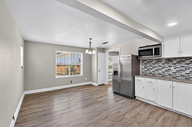 Kitchen featuring appliances with stainless steel finishes, tasteful backsplash, light wood finished floors, a chandelier, and white cabinetry | Image 24