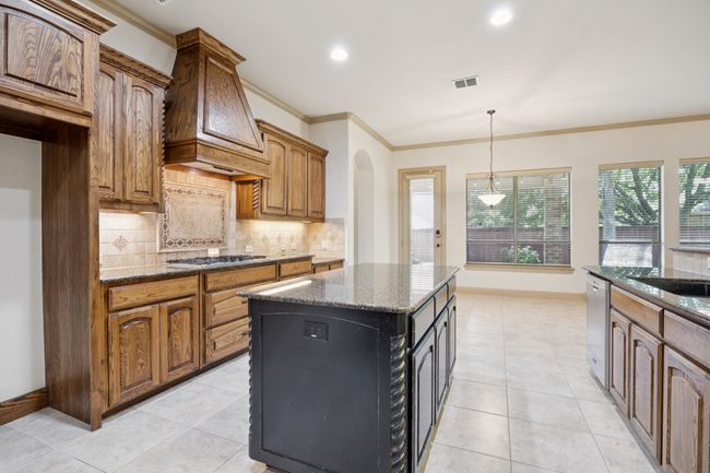 Kitchen featuring ornamental molding, custom exhaust hood, dark stone counters, appliances with stainless steel finishes, and tasteful backsplash | Image 16
