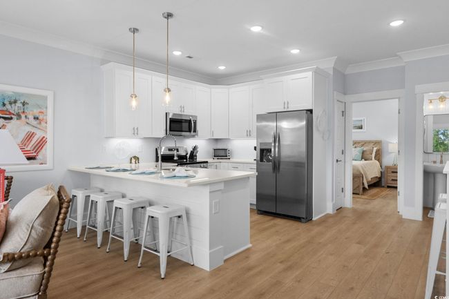 Kitchen with a kitchen breakfast bar, stainless steel appliances, white cabinetry, a peninsula, and crown molding | Image 11