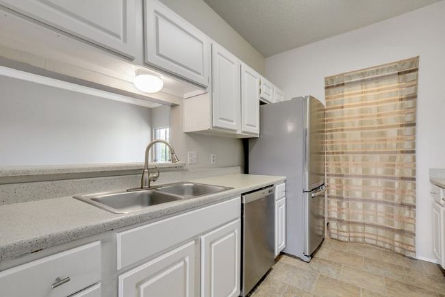Kitchen with stainless steel appliances and open window into living room. | Image 7