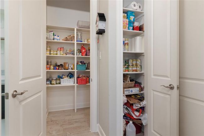 This photo showcases a well-organized pantry with ample shelving for storing food items and supplies. Two doors open to reveal multiple shelves that will hold all of your various kitchen essentials. The space is bright and functional, ideal for keeping your kitchen organized. | Image 17