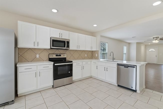 Kitchen with appliances with stainless steel finishes, a sink, a peninsula, light countertops, and decorative backsplash | Image 7