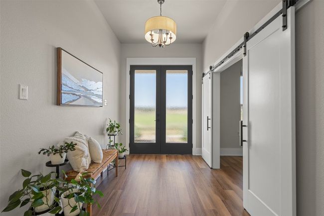 Foyer entrance with a barn door, french doors, wood finished floors, a chandelier, and baseboards | Image 19