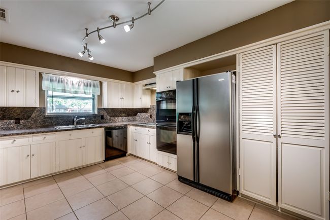 Kitchen featuring light tile patterned flooring, visible vents, tasteful backsplash, a sink, and black appliances | Image 9