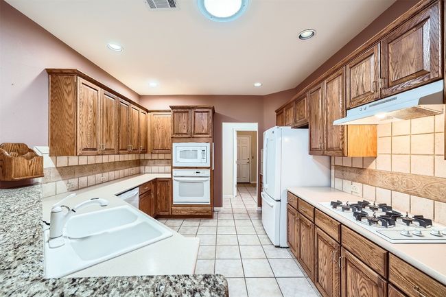 Kitchen featuring white appliances, under cabinet range hood, light countertops, brown cabinets, and recessed lighting | Image 13