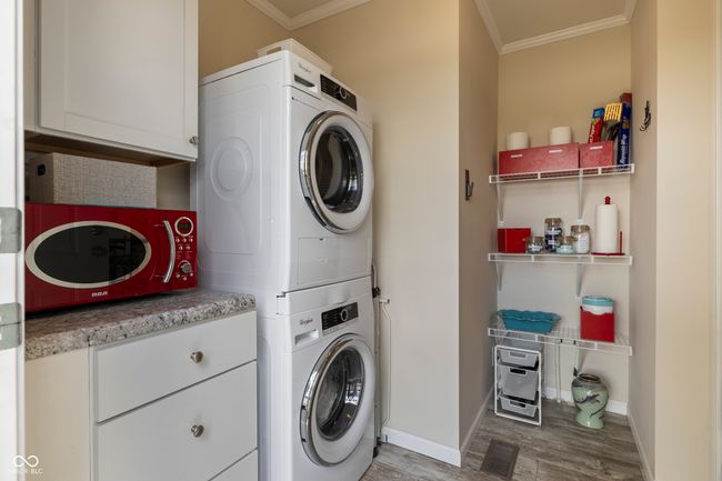 laundry area with stacked washer / drying machine, ornamental molding, cabinet space, wood finished floors, and baseboards | Image 31