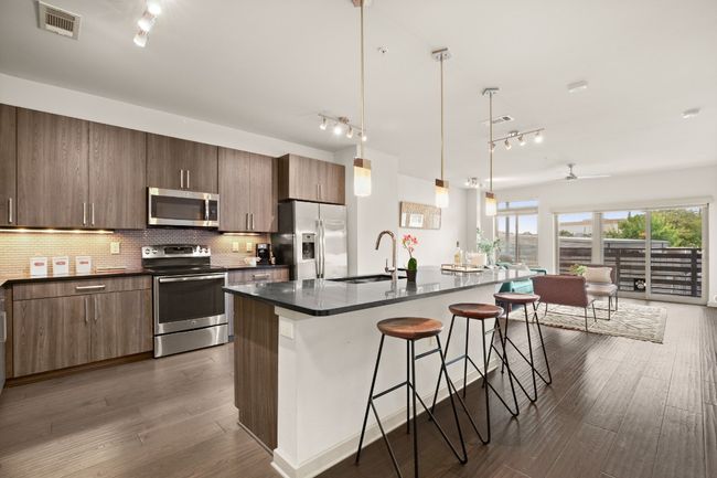 Kitchen featuring appliances with stainless steel finishes, track lighting, dark countertops, a kitchen breakfast bar, and a sink | Image 25