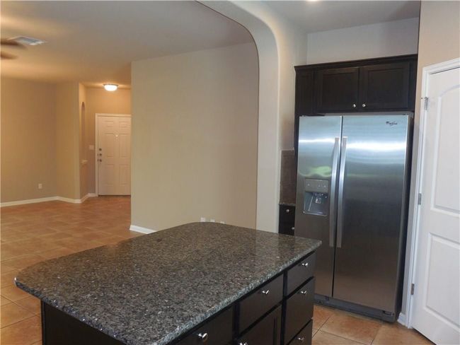 Kitchen with stainless steel fridge with ice dispenser, light tile patterned floors, arched walkways, dark stone countertops, and a kitchen island | Image 6
