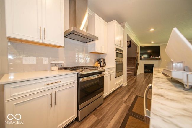 kitchen with appliances with stainless steel finishes, wall chimney range hood, white cabinets, light countertops, and decorative backsplash | Image 10