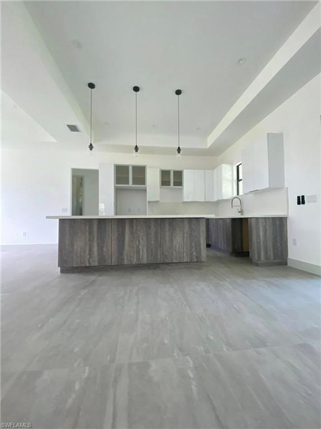 Modern Gourmet Kitchen:Bright and airy with sleek white cabinetry, a textured wood-look island, quartz countertops, and stylish pendant lighting under soaring tray ceilings. Perfect for casual dining and elegant entertaining. | Image 8