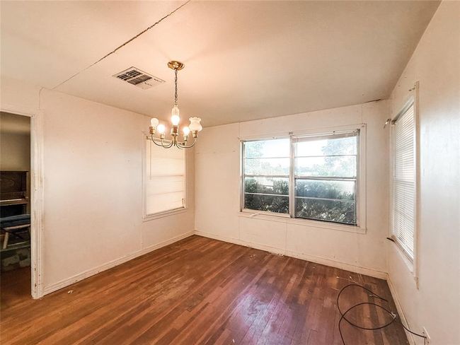 This dining room features hardwood flooring, dual large windows allowing natural light, and a central chandelier. Ideal for a dining area or versatile living space. Some updates may enhance its charm. | Image 8