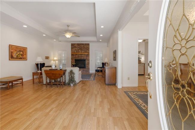 Living room featuring baseboards, light wood-style flooring, a ceiling fan, a brick fireplace, and a tray ceiling | Image 8