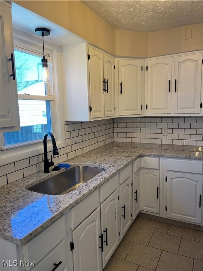 Kitchen featuring white cabinetry, granite counters, backsplash, a sink and a new light. | Image 5