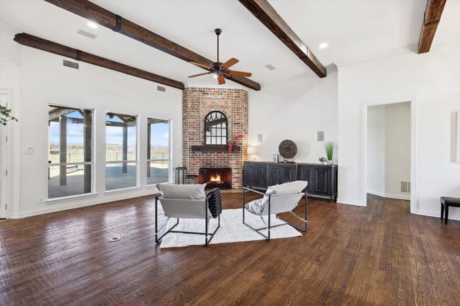 Living room with a ceiling fan, beamed ceiling, dark wood finished floors, a brick fireplace, and baseboards | Image 7